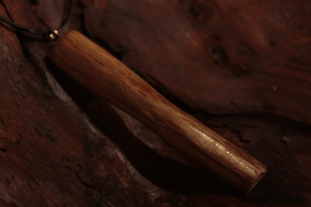 Pendentif bâtonnet en bois clair, sur une écorce sombre